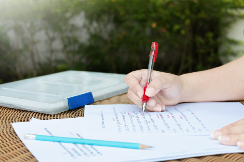 Person holding a red pen editing a piece of writing