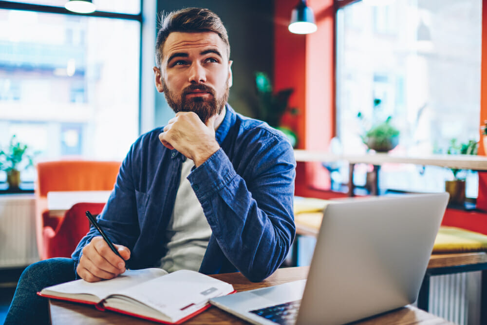 Man sitting in front of his laptop with a notebook and pen
